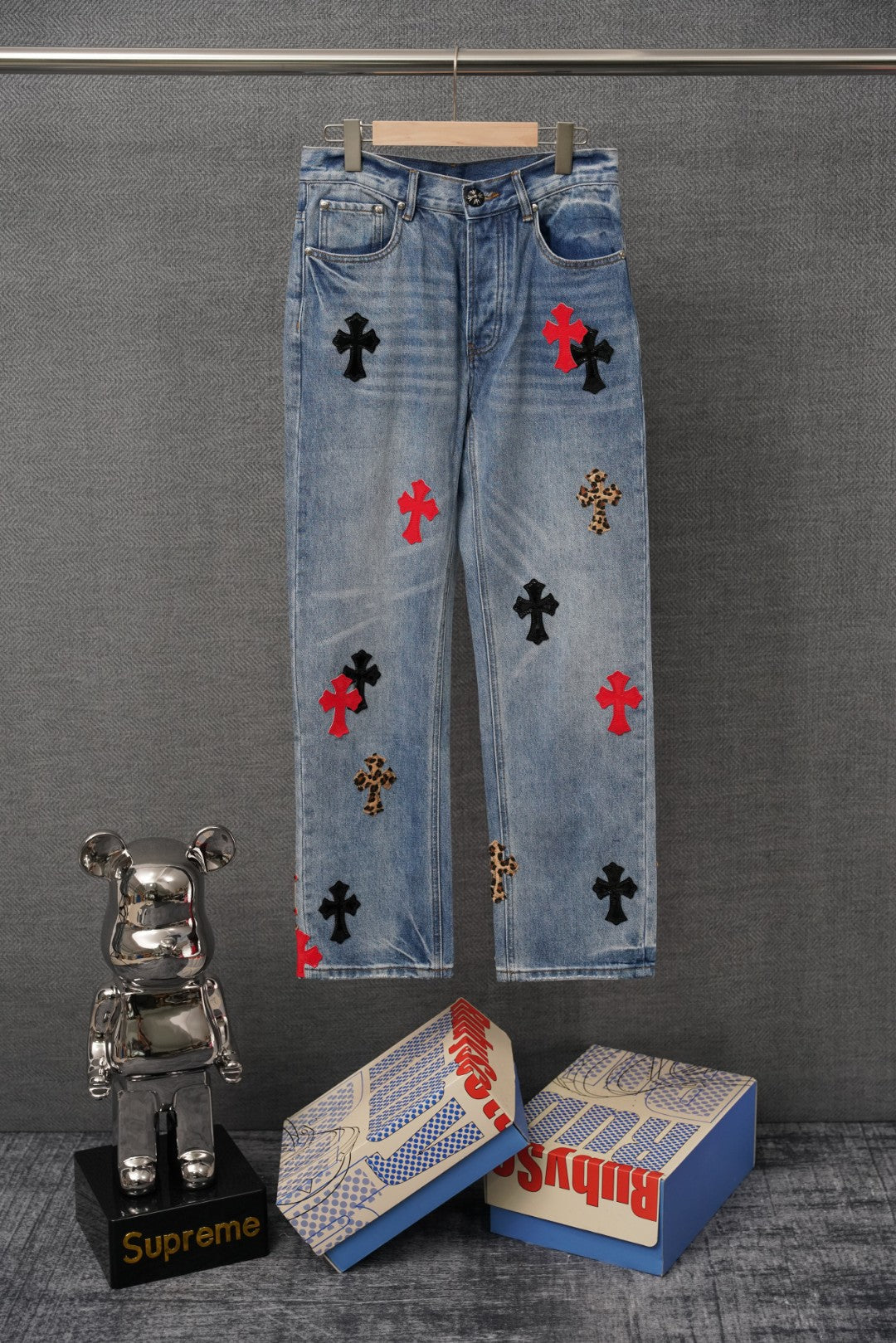 Light blue denim pants with scattered cross patches, front view on hanger