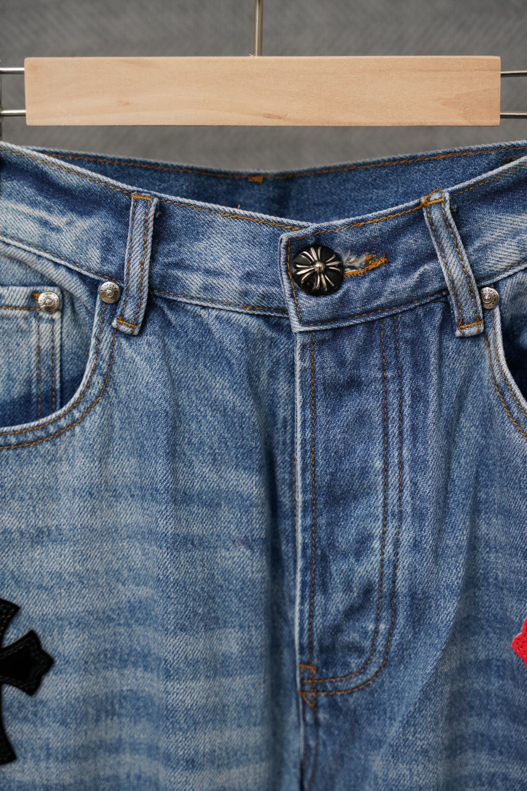 Light blue denim pants waistband and back pocket with small cross emblem detail.