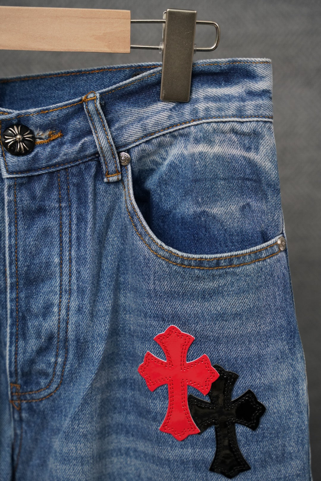 Light blue denim pants with red and black cross patch, front pocket area.