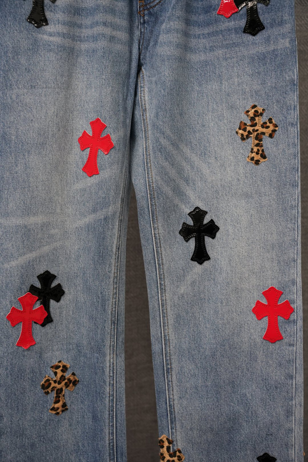 Light blue denim pants side view with red, leopard, and black cross patches.