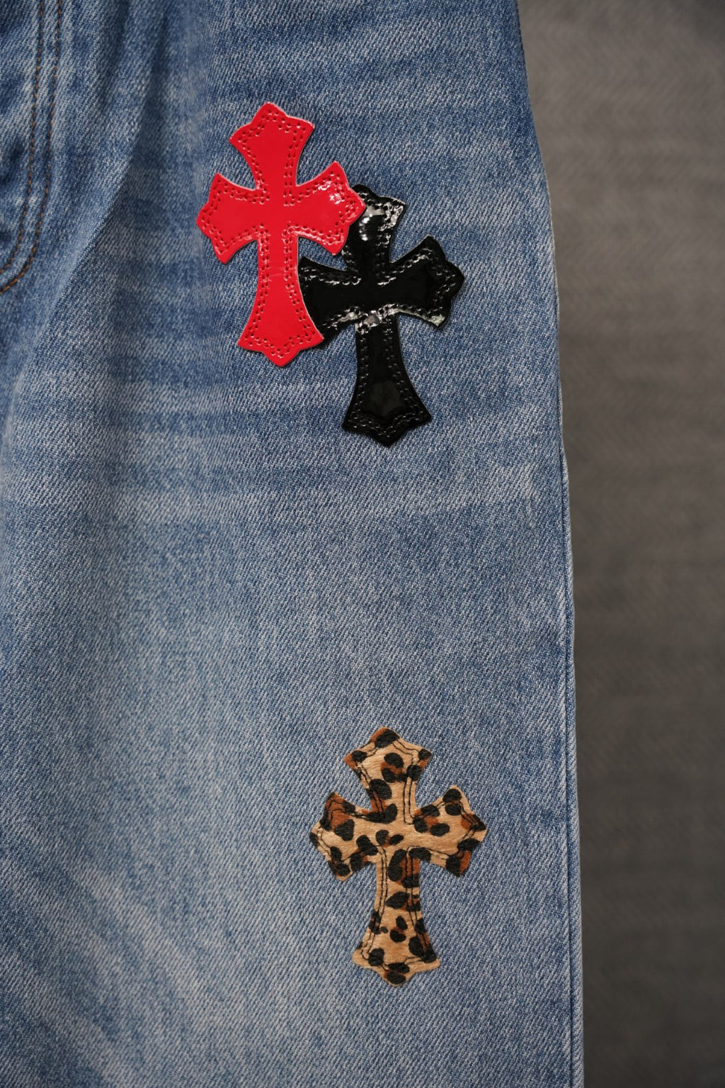 Light blue denim with red and black cross patches and leopard-print cross near hem.