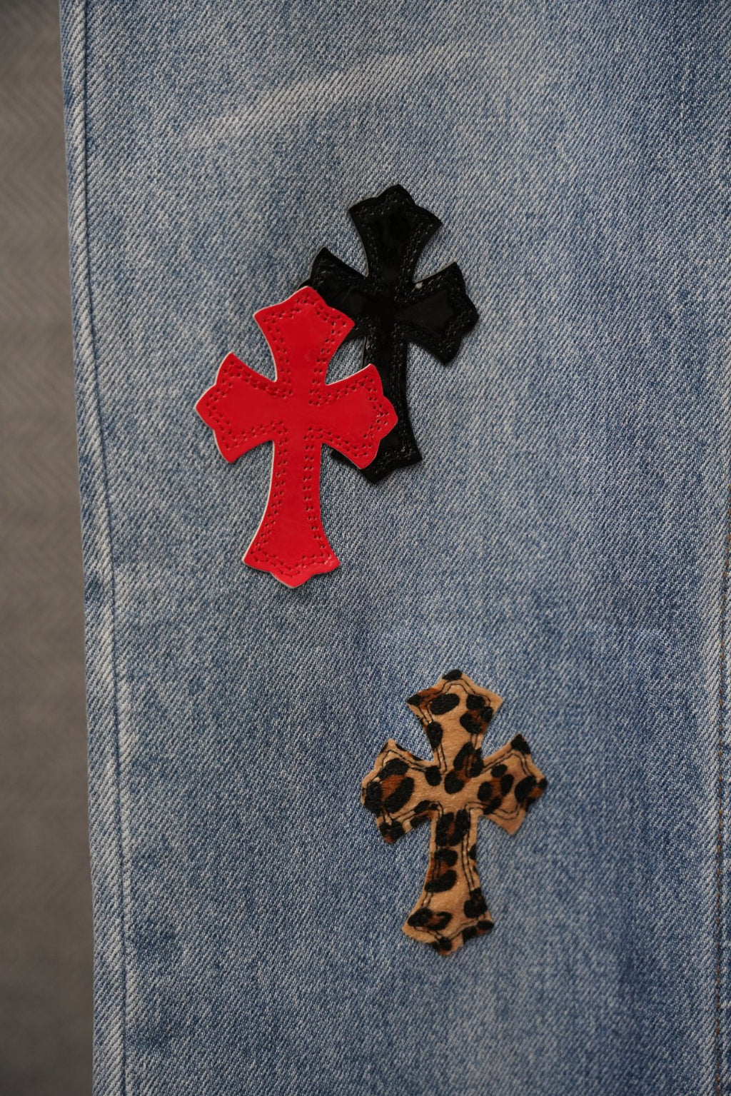 Light blue denim with red and black cross patches and leopard-print cross.