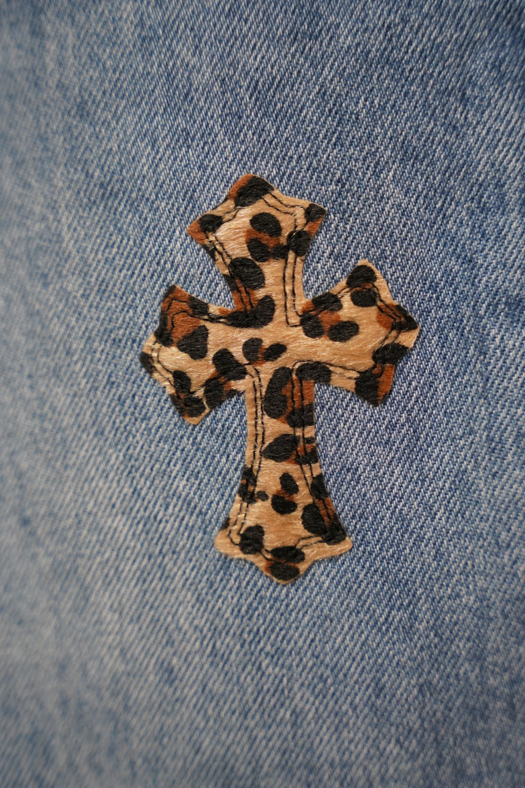 Light blue denim pants close-up of leopard-print cross patch on fabric