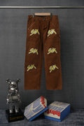 Brown cargo pants with embroidered green “S€X” graphic on front legs