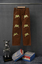 Brown cargo pants with embroidered green “S€X” graphic on front legs