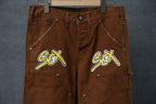 Front view of brown cargo pants with two neon “Sex” graphic patches