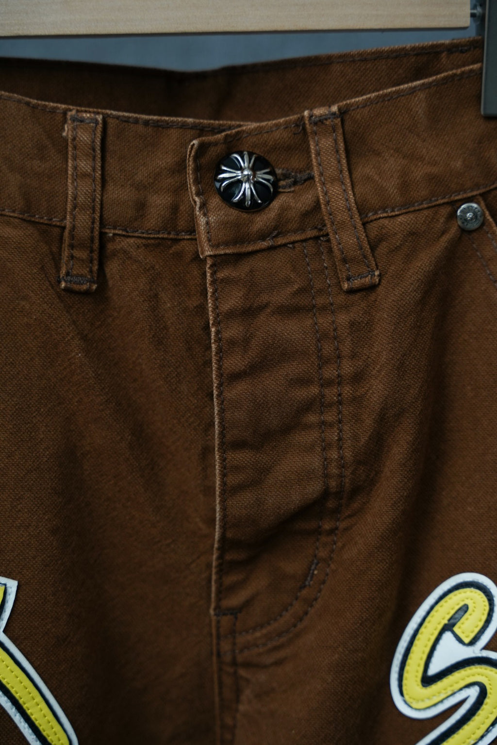 Brown cargo pants waist with button closure and neon “Sex” patch on pocket