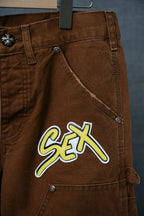 Brown cargo pants with front pocket and large neon “Sex” patch