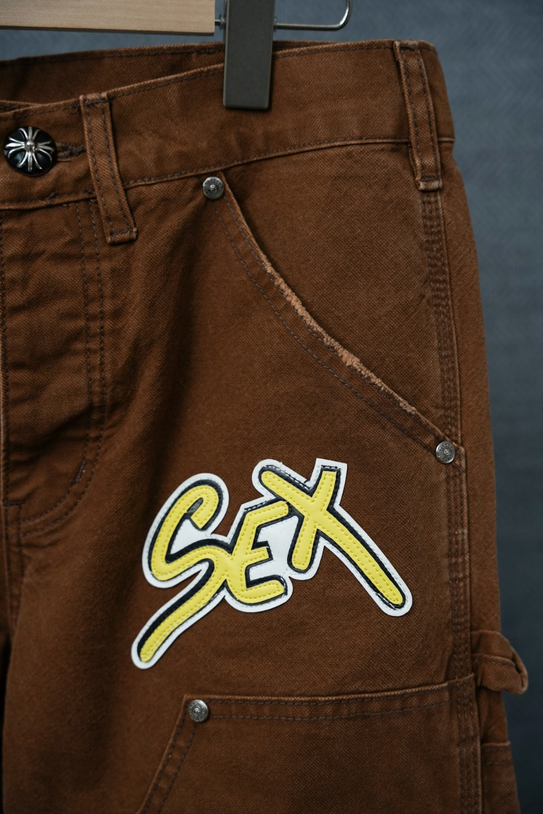 Brown cargo pants with front pocket and large neon “Sex” patch