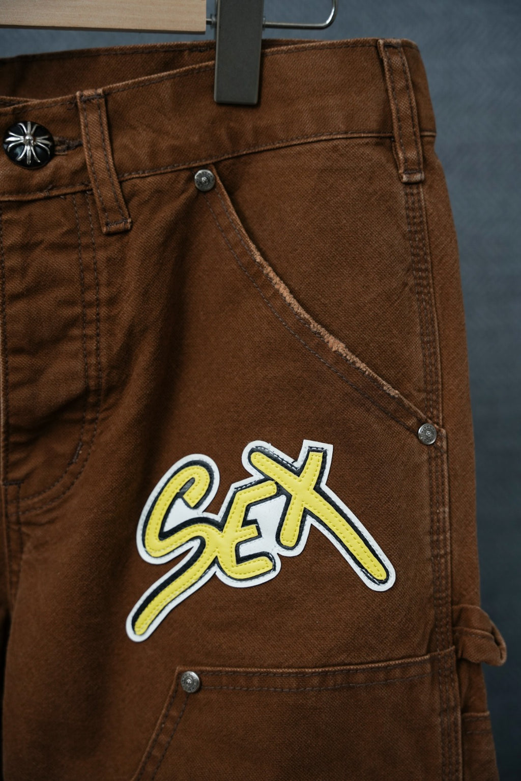 Brown cargo pants front close-up showing large “S€X” embroidered graphic patch