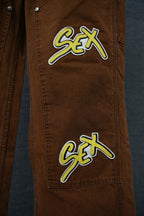 Brown cargo pants with neon “Sex” patch on thigh and side seam details