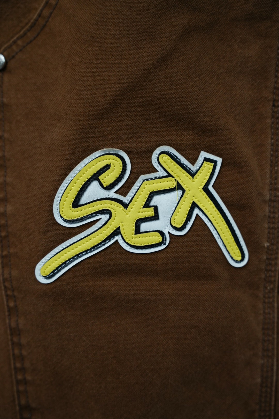 Close-up of brown cargo pants fabric with neon “Sex” patch