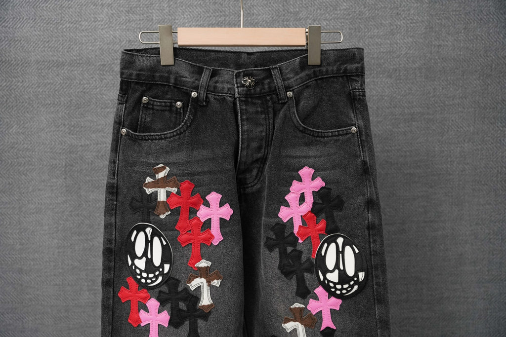 Dark denim pants with embroidered cross and skull patches, front view