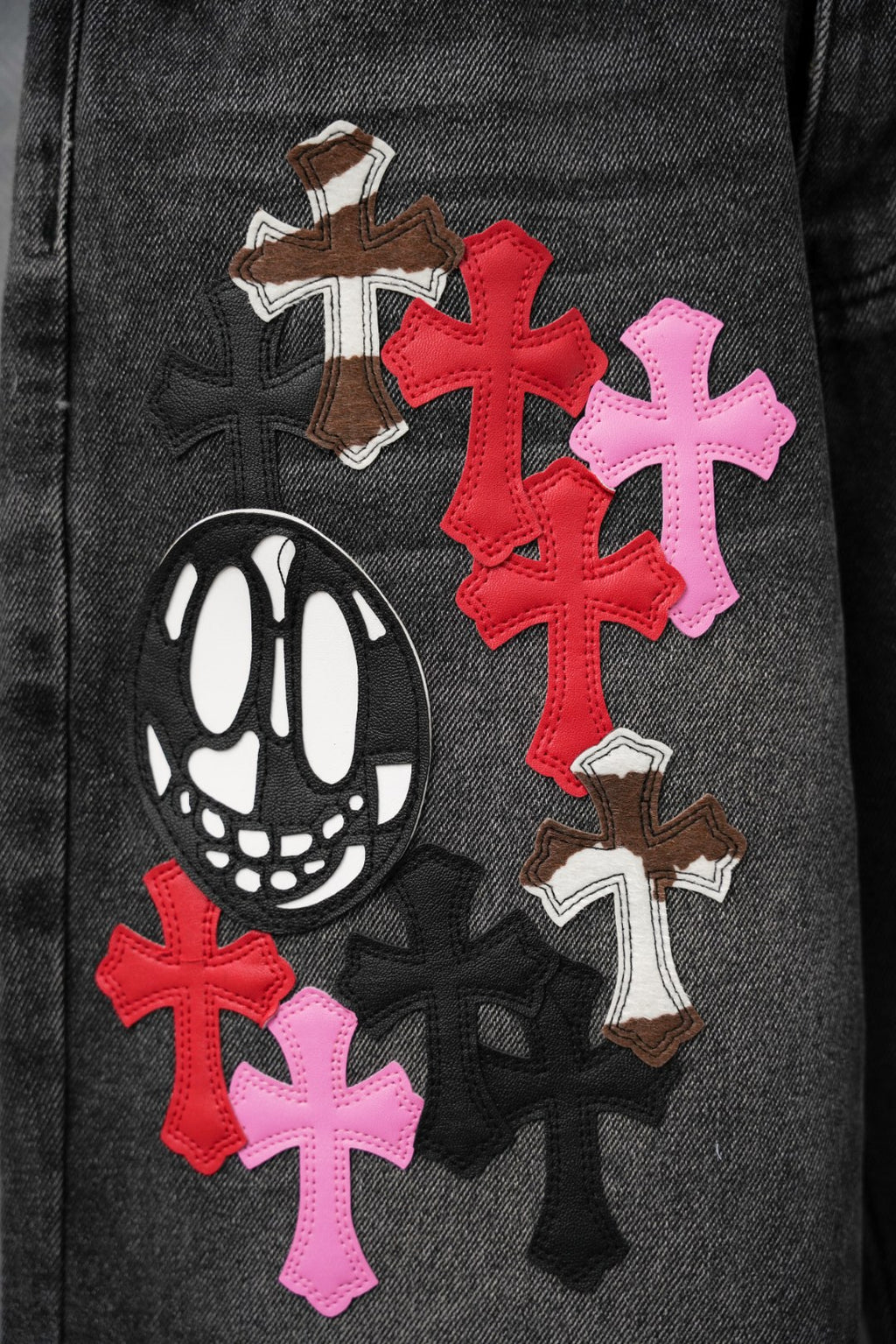 Black denim pants leg with red, pink, and brown cross patches and cartoon face