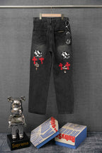 Dark denim pants with embroidered cross patches and skull graphic on back