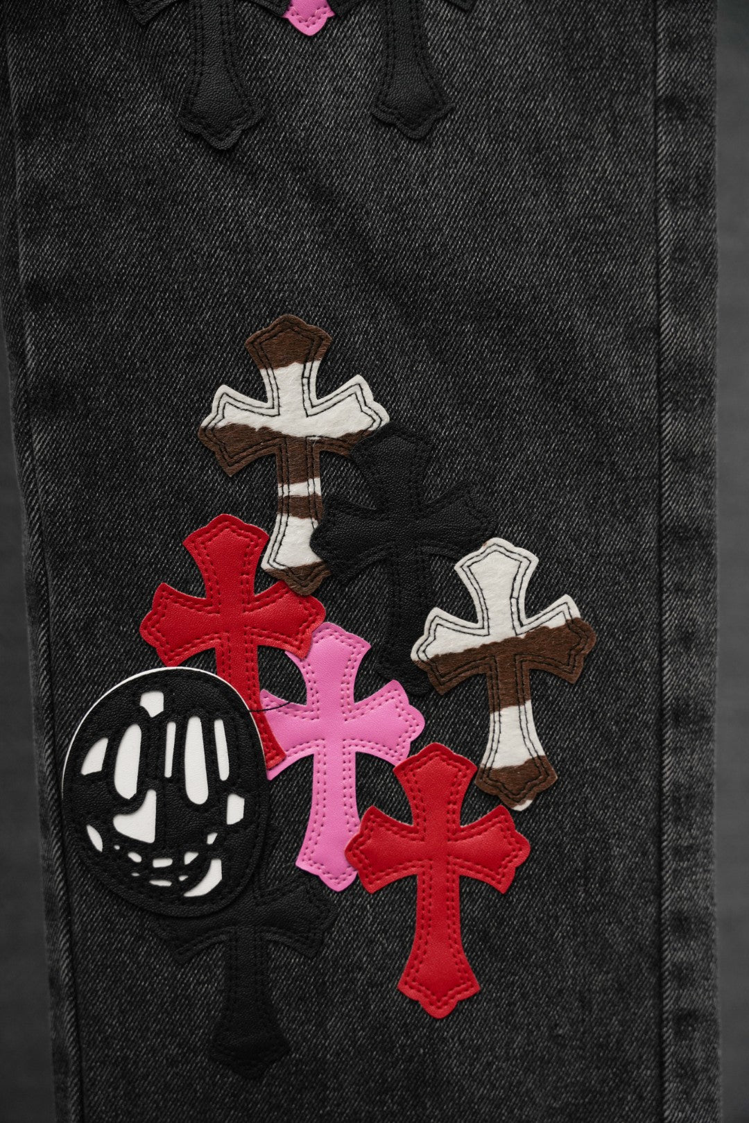 Black denim pants with stacked cross patches in red, pink, brown, and white
