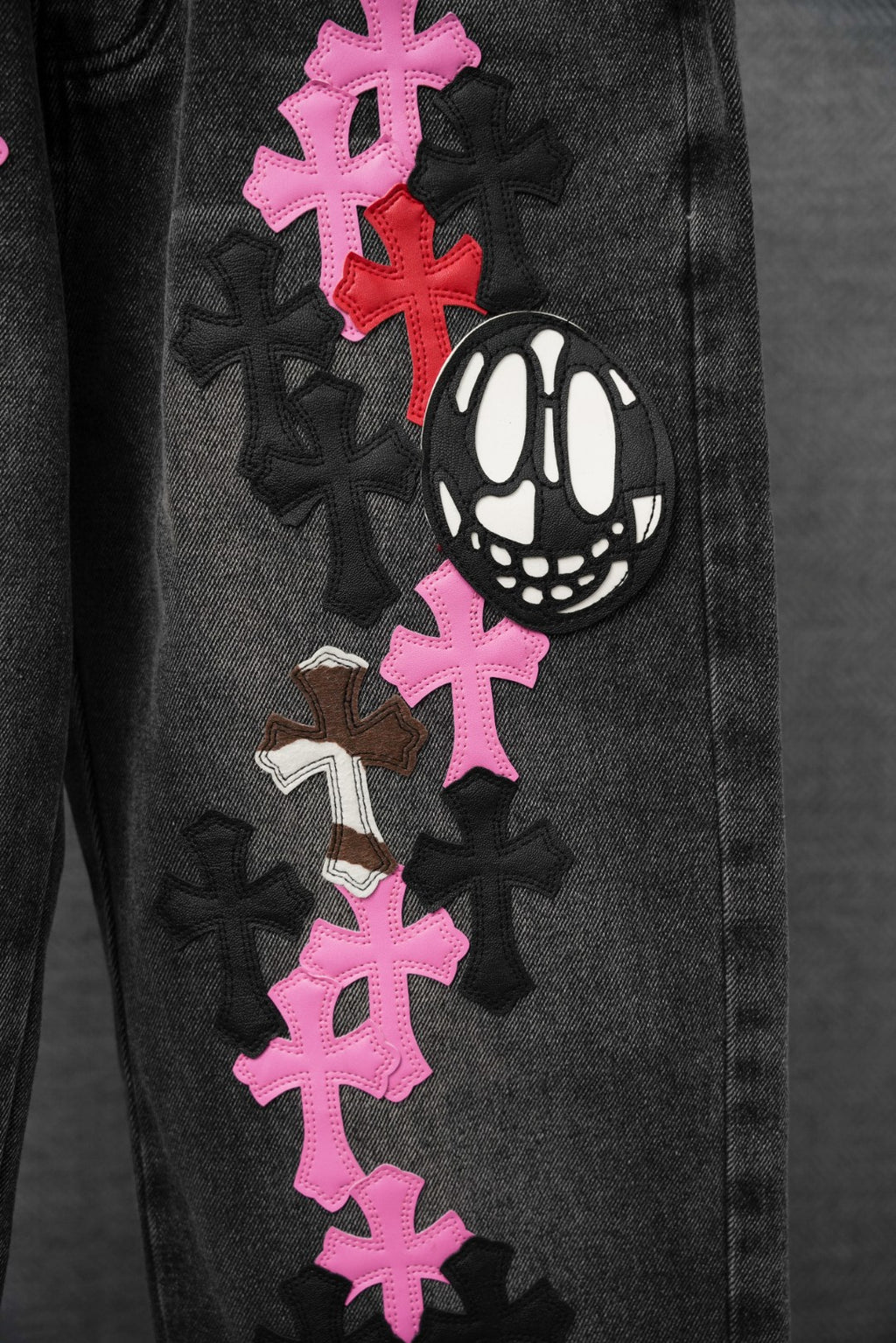Black denim pants leg with pink cross patches and black cartoon face emblem