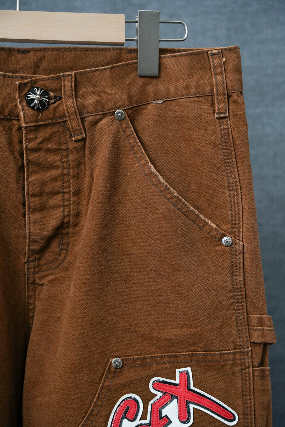 Brown cargo pants with cargo pocket and stitched seam lines; “Sex” graphic near hem