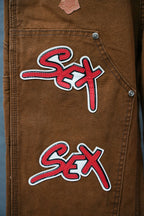 Brown cargo pants close-up showing stacked “Sex” graffiti patches on pocket