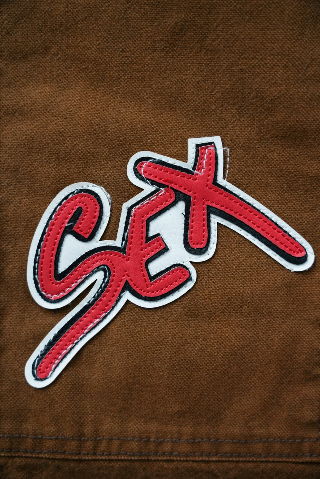 Brown cargo pants close-up of red-and-white “Sex” graffiti patch on fabric