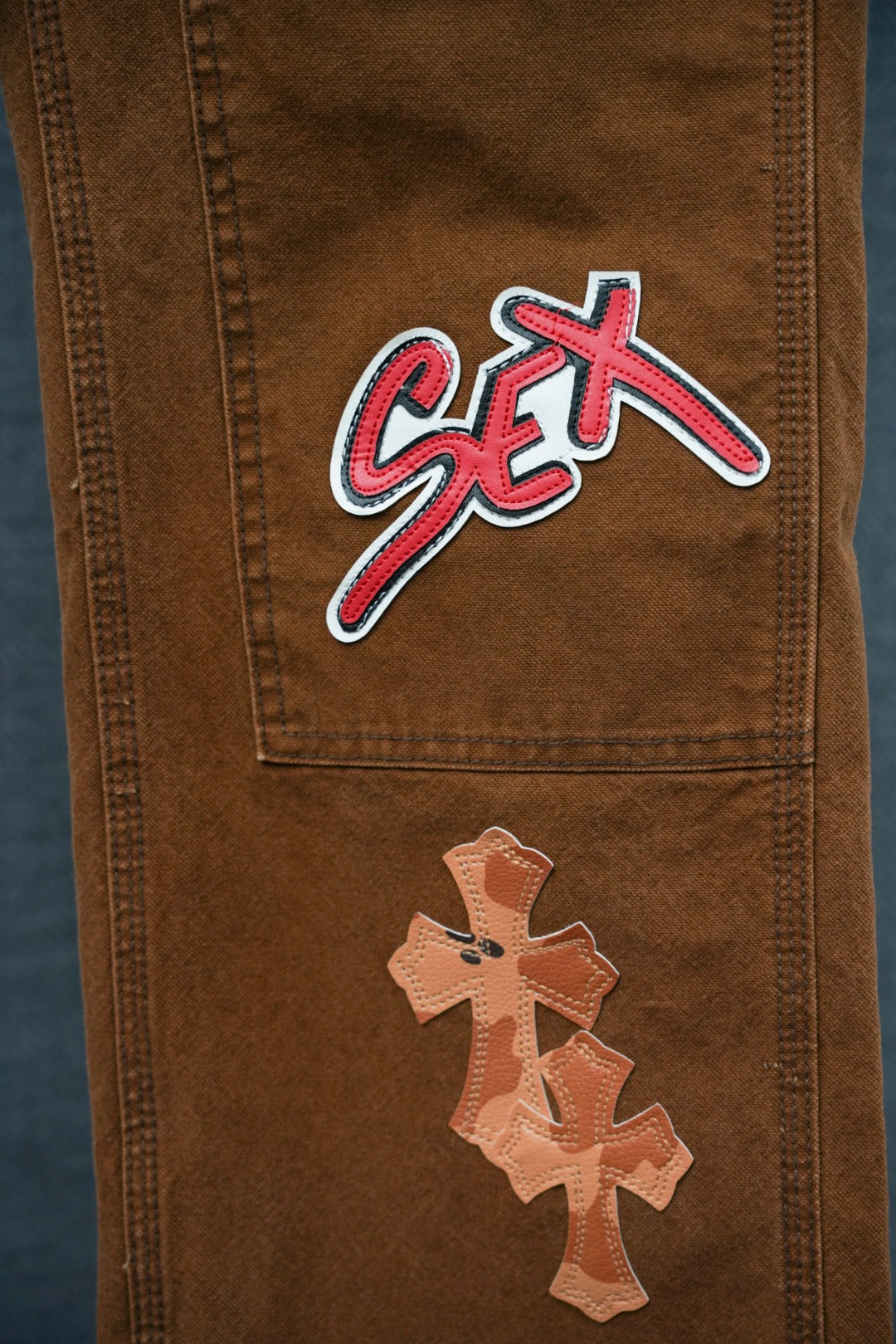 Brown cargo pants with “SEX” patch and cross applique on lower panel