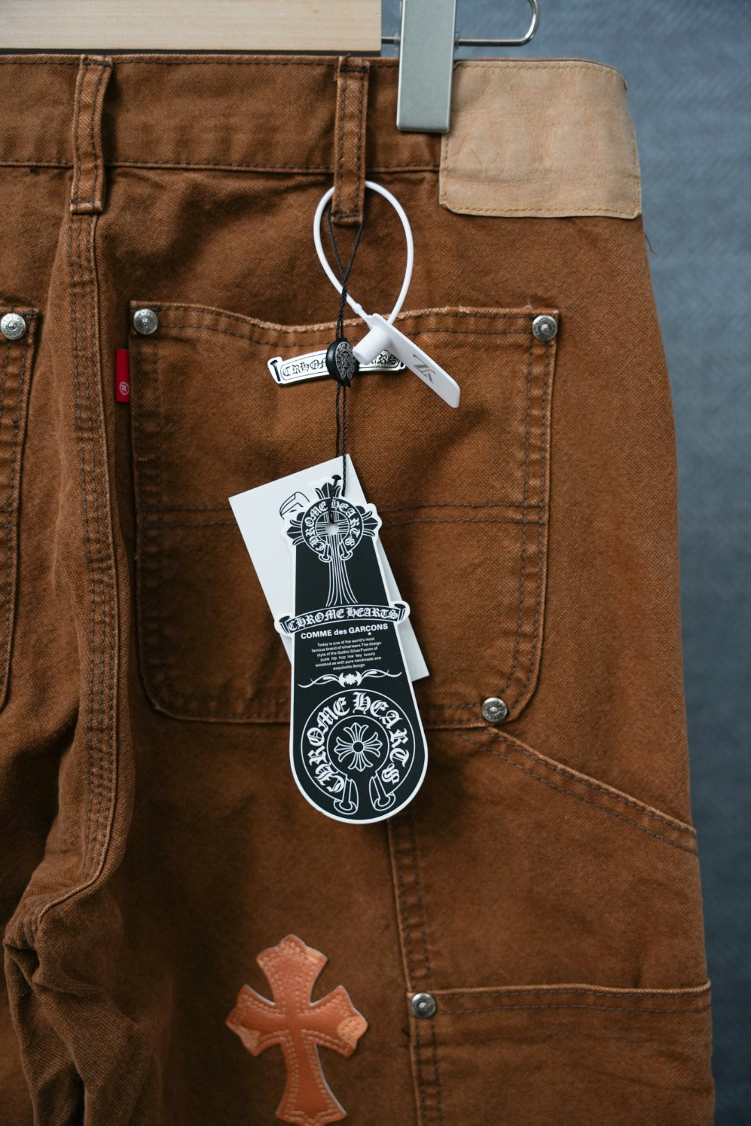 Brown cargo pants with multiple orange cross appliques and dangling tag