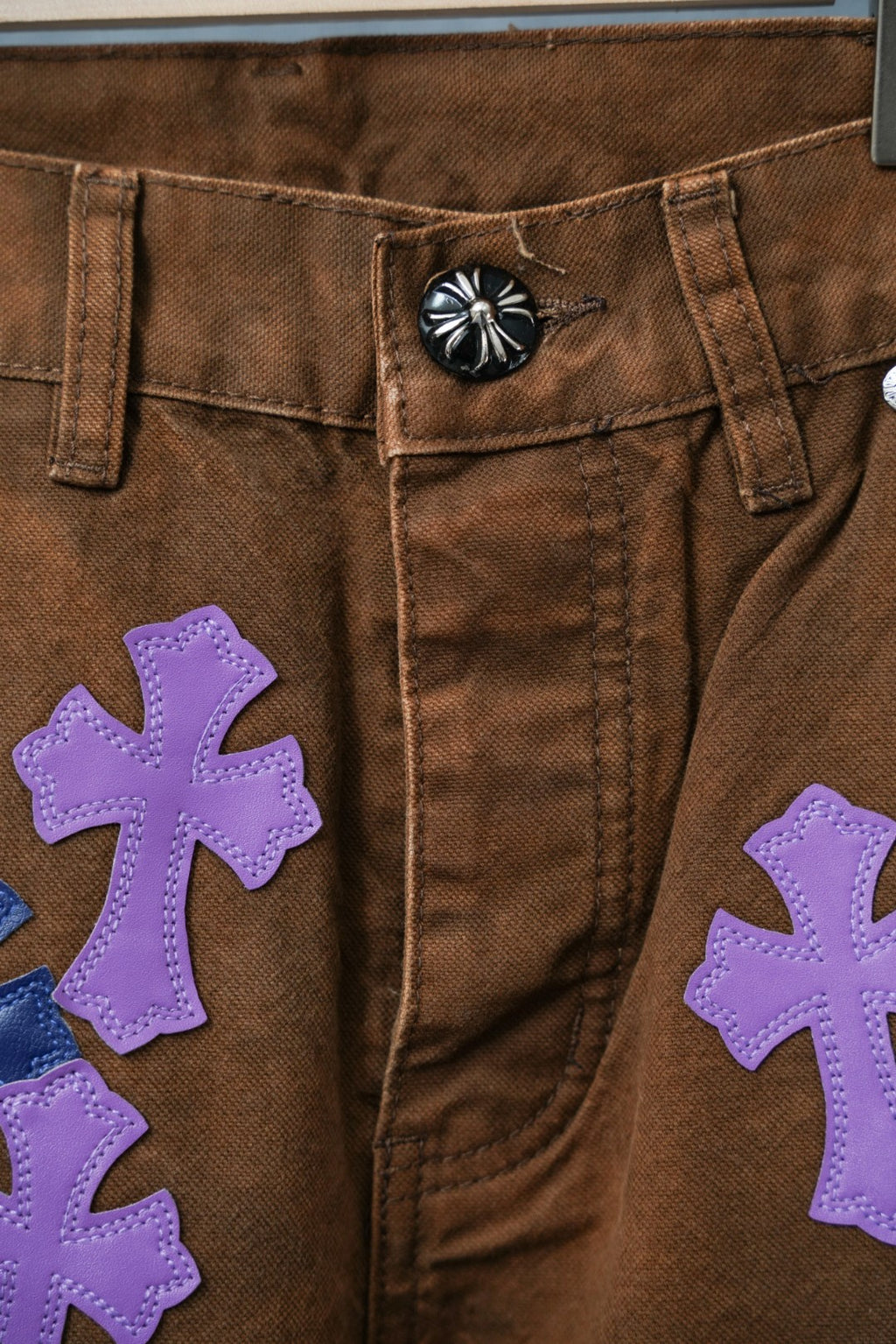 Close-up of brown jeans front with large purple cross patch detail