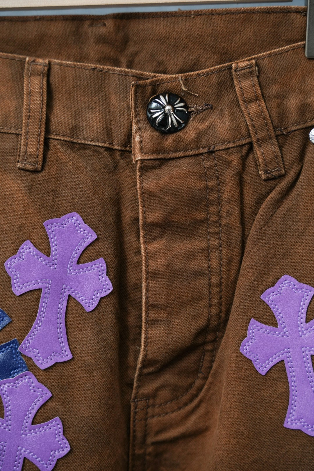 Close-up of brown jeans front with large purple cross patch detail