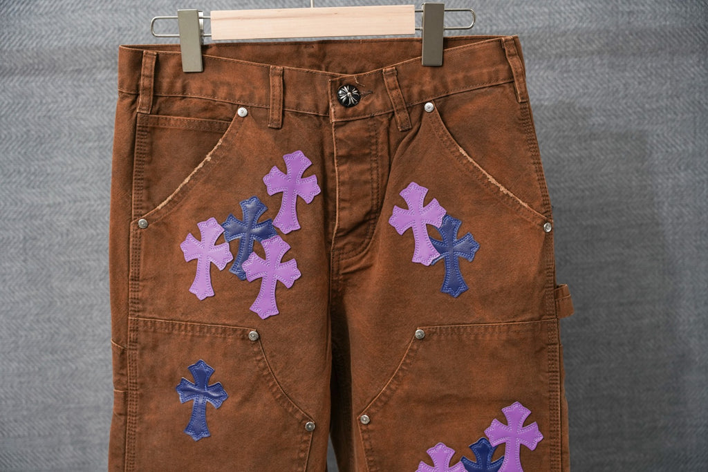 Brown denim pants with blue and purple cross appliques on front pockets
