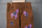 Brown denim pants with blue and purple cross appliques on front pockets