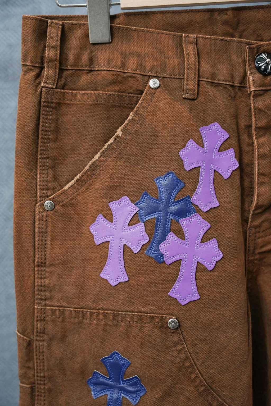 Close-up of brown jeans with purple and blue cross patch cluster