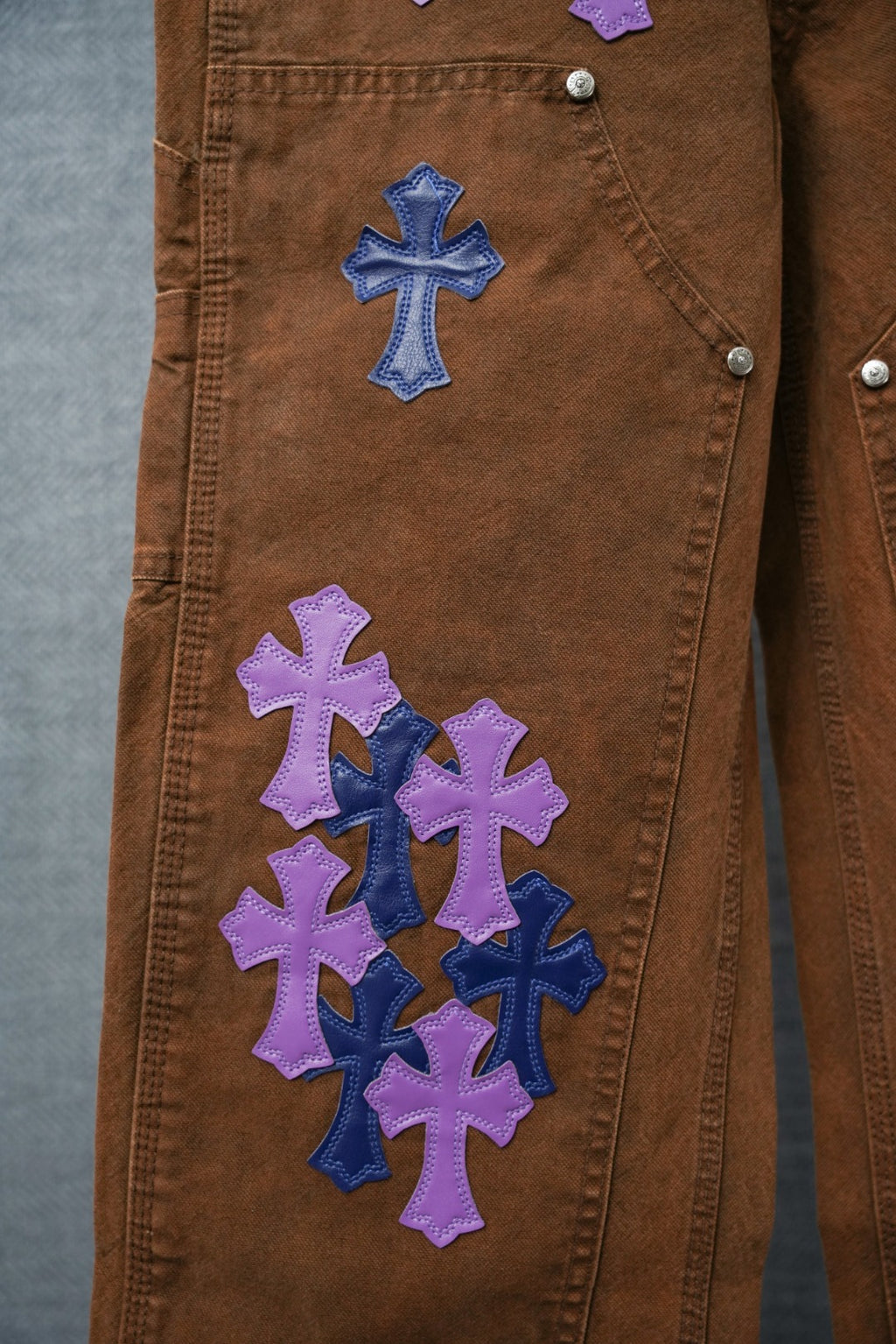 Brown denim leg with blue and purple embroidered cross patches