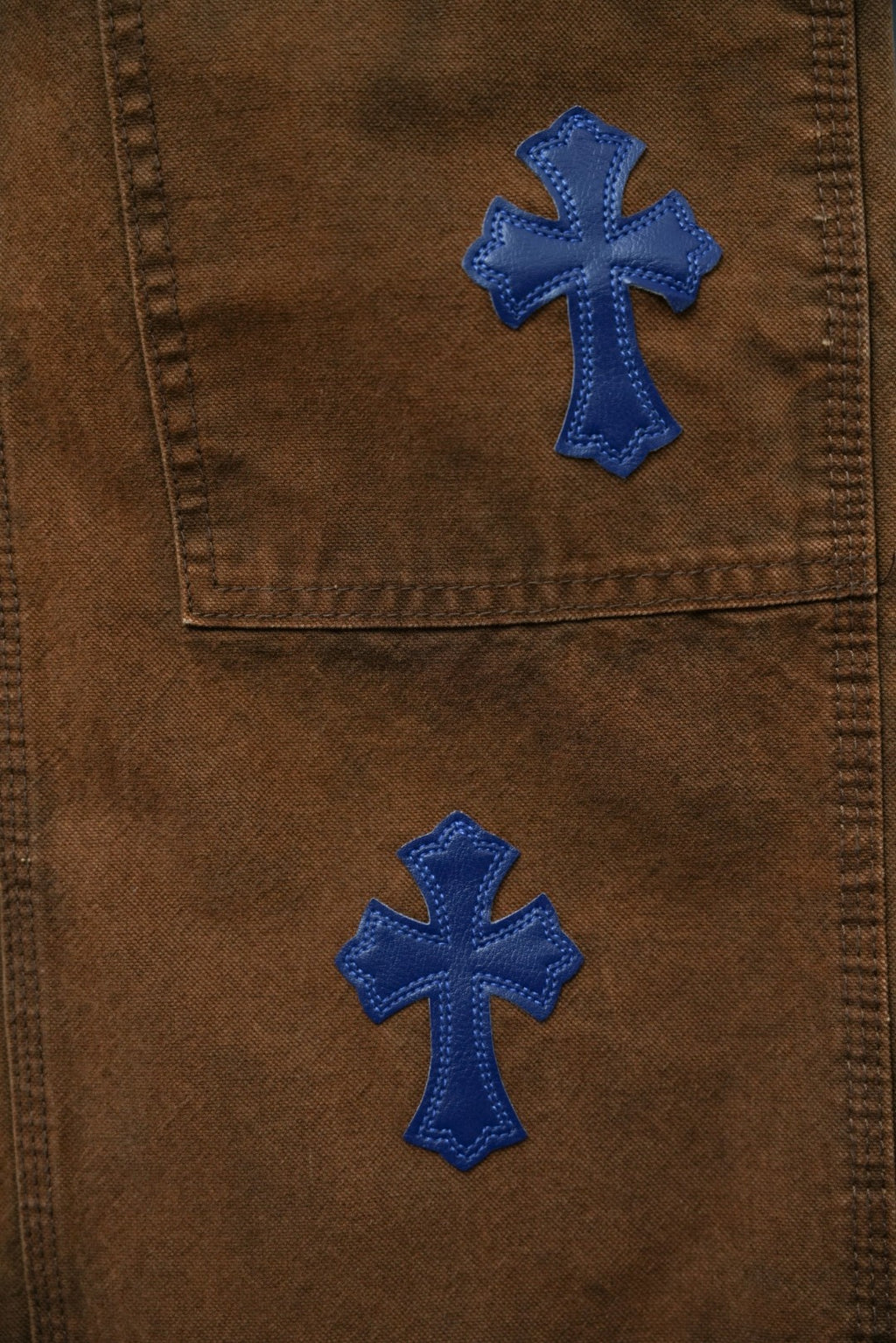 Brown denim pants with blue embroidered cross patches on front panels
