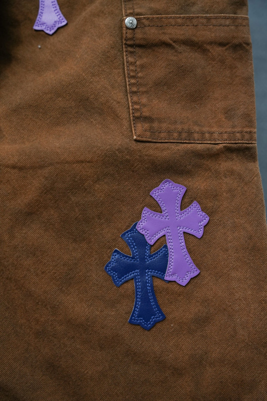 Brown pants with purple and blue cross patches; stitched pocket corner visible