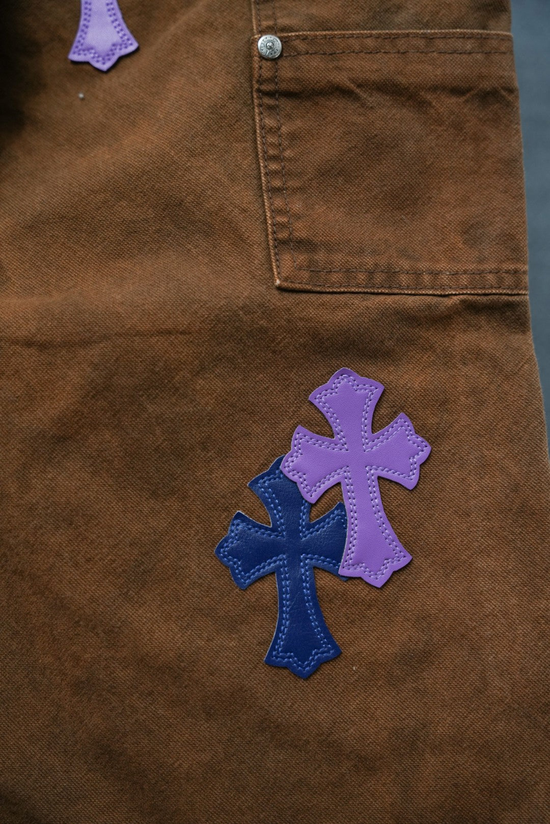 Brown pants with purple and blue cross patches; stitched pocket corner visible