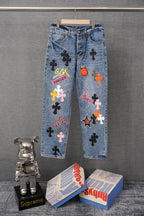 Blue denim pants with colorful graphic patches and belt loops, front view.