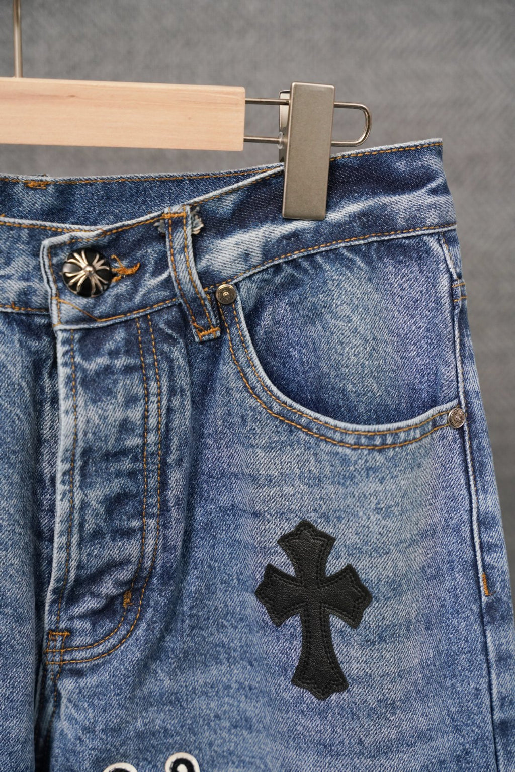 Blue denim pants with coin pocket and black cross patch, close-up.