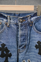 Blue denim pants center front with button and black cross patches, close-up.