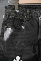Black denim pants with front coin pocket and embossed cross appliques, close-up