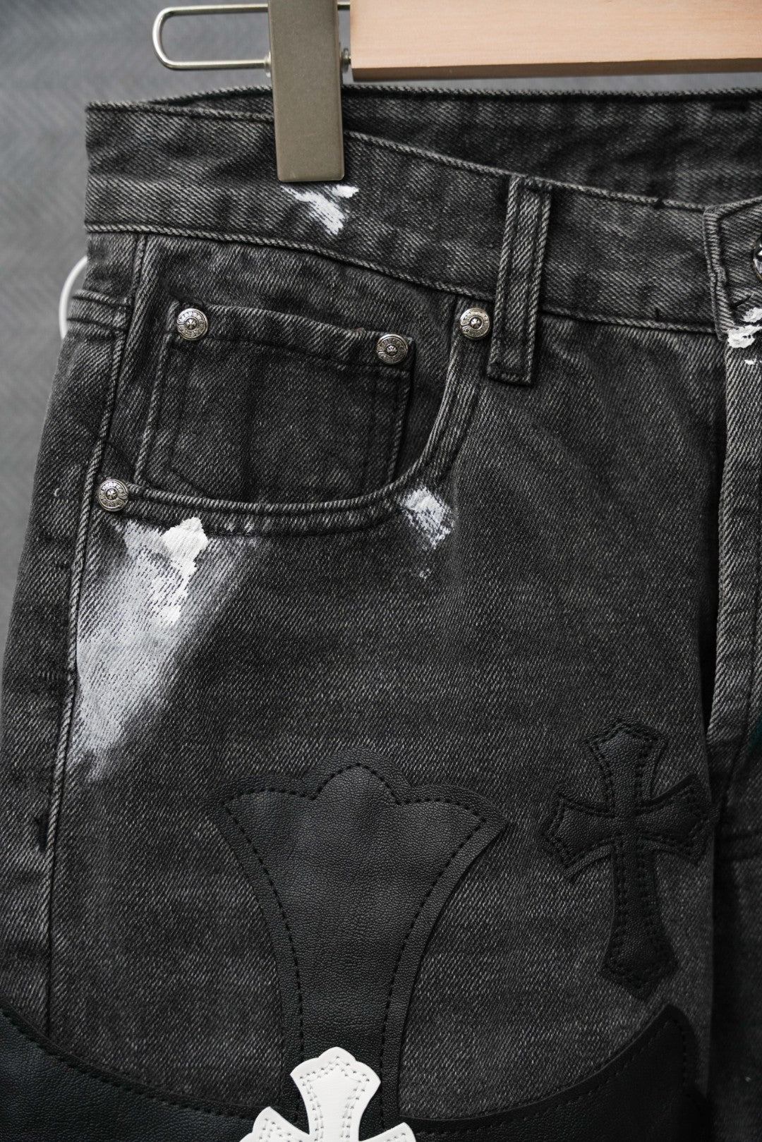 Black denim pants with front coin pocket and embossed cross appliques, close-up
