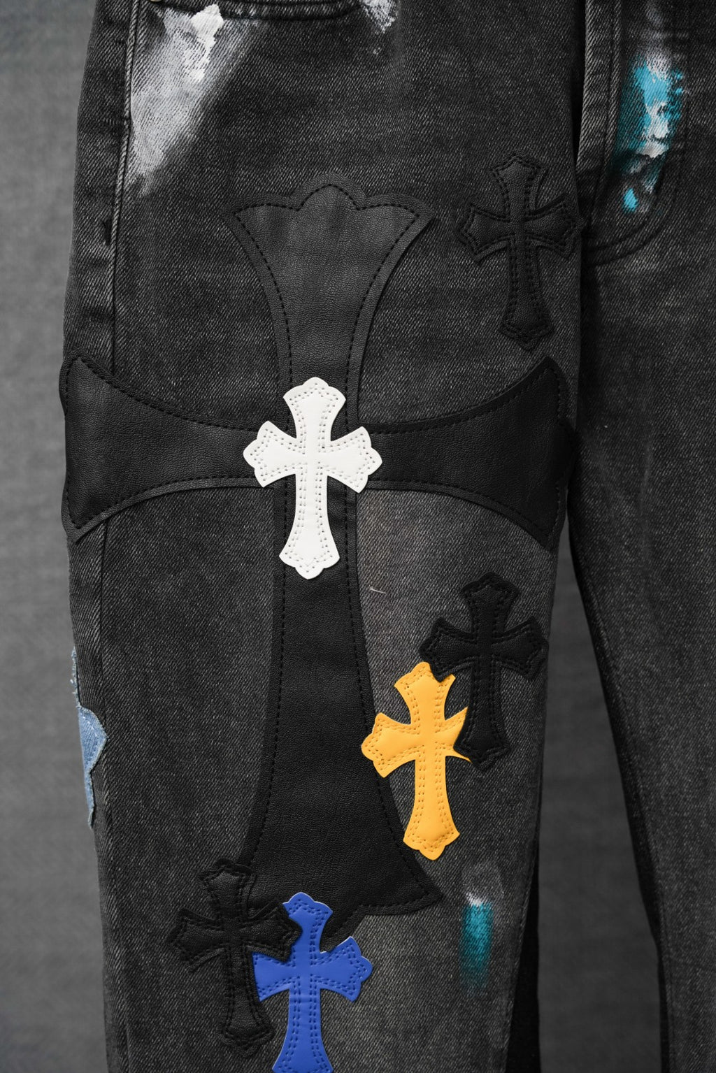 Black denim pants with large white cross patch and smaller colored cross details