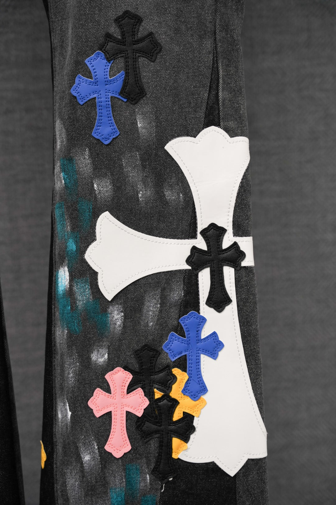 Black denim pants with colorful cross appliques on knee and thigh, close-up