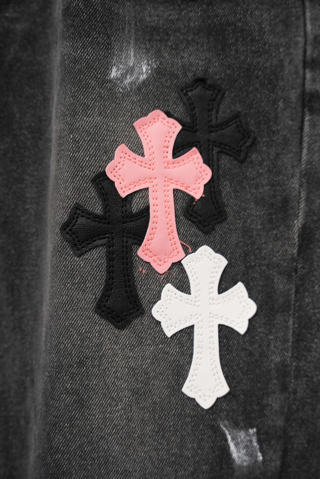 Black denim pants fabric with pink and white cross patches, close-up