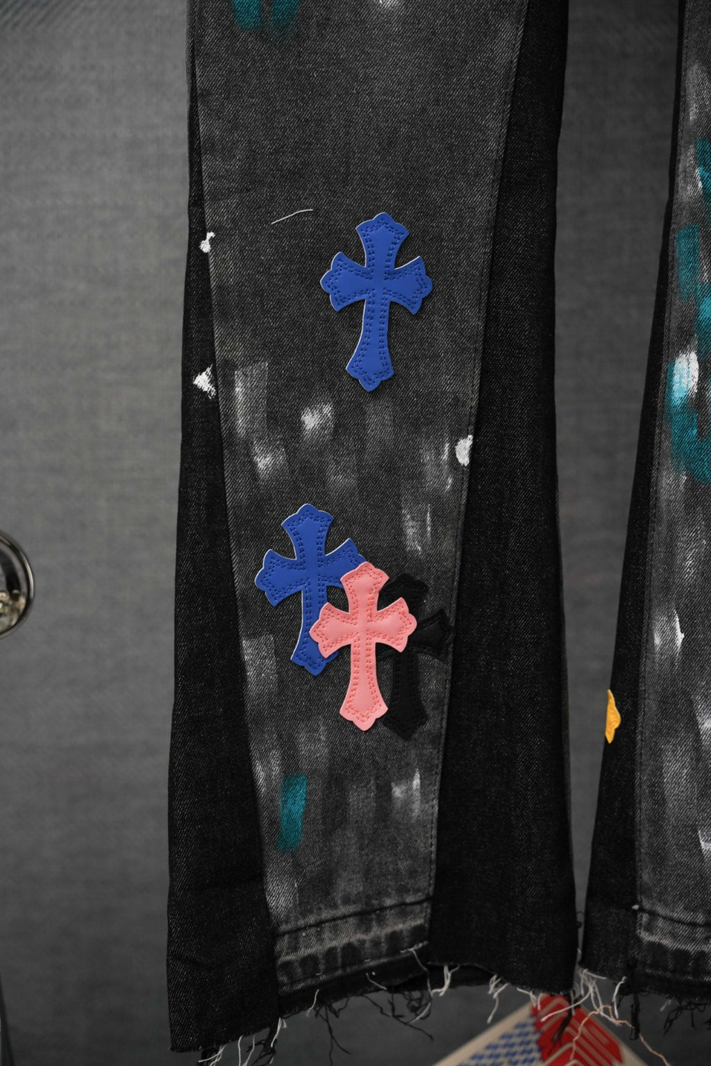 Side view of dark denim pants with blue and pink cross appliques