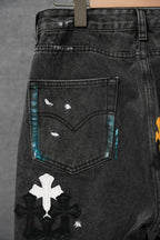 Black denim pants close-up: stitched front pocket with cross patch accents