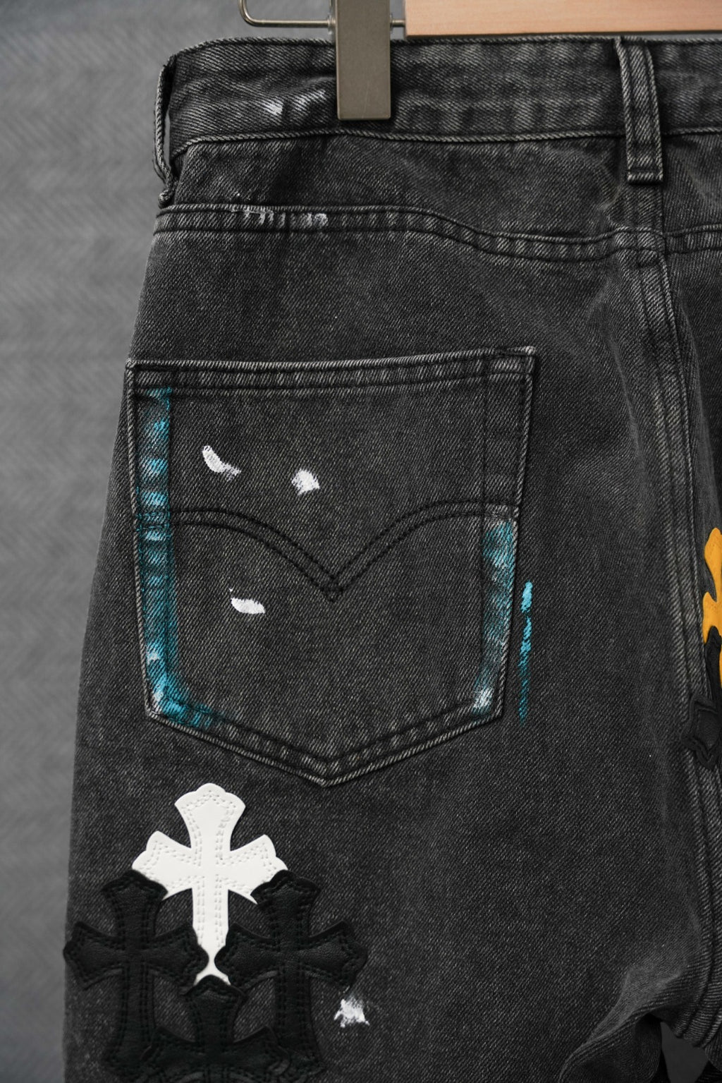 Dark denim pants with front pocket panel and colorful cross patches along the thigh