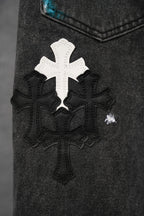 Black denim pants close-up: white cross applique with dark floral detail