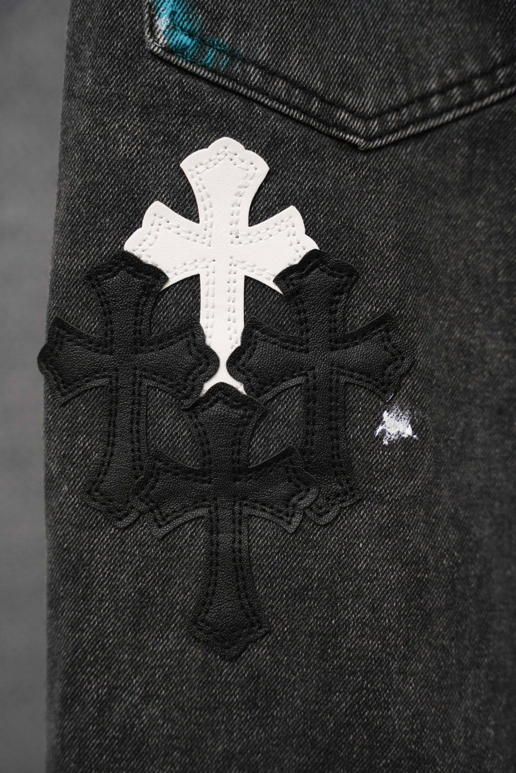 Dark denim pants with a large white cross applique and black patterned embroidery