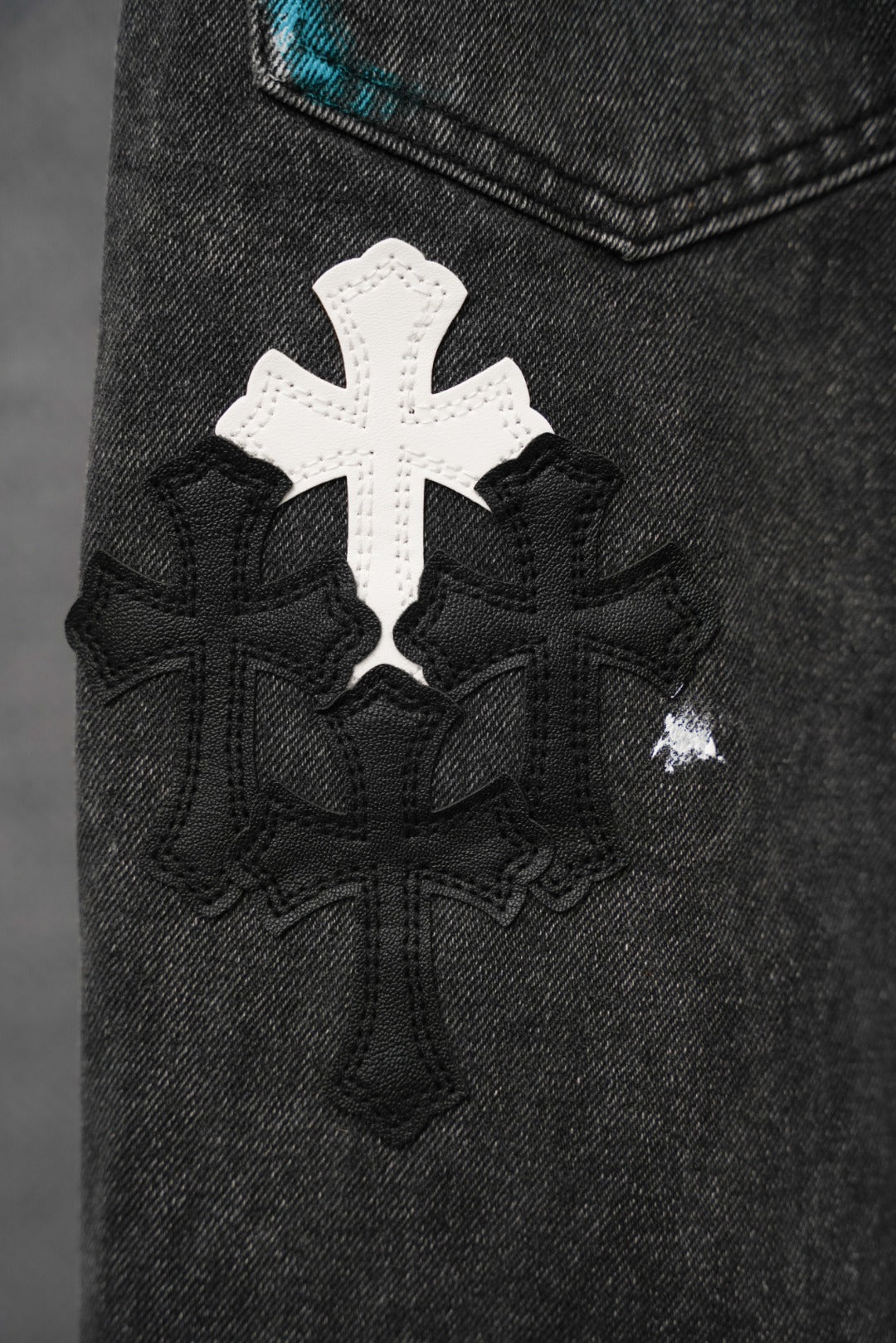 Dark denim pants with a large white cross applique and black patterned embroidery