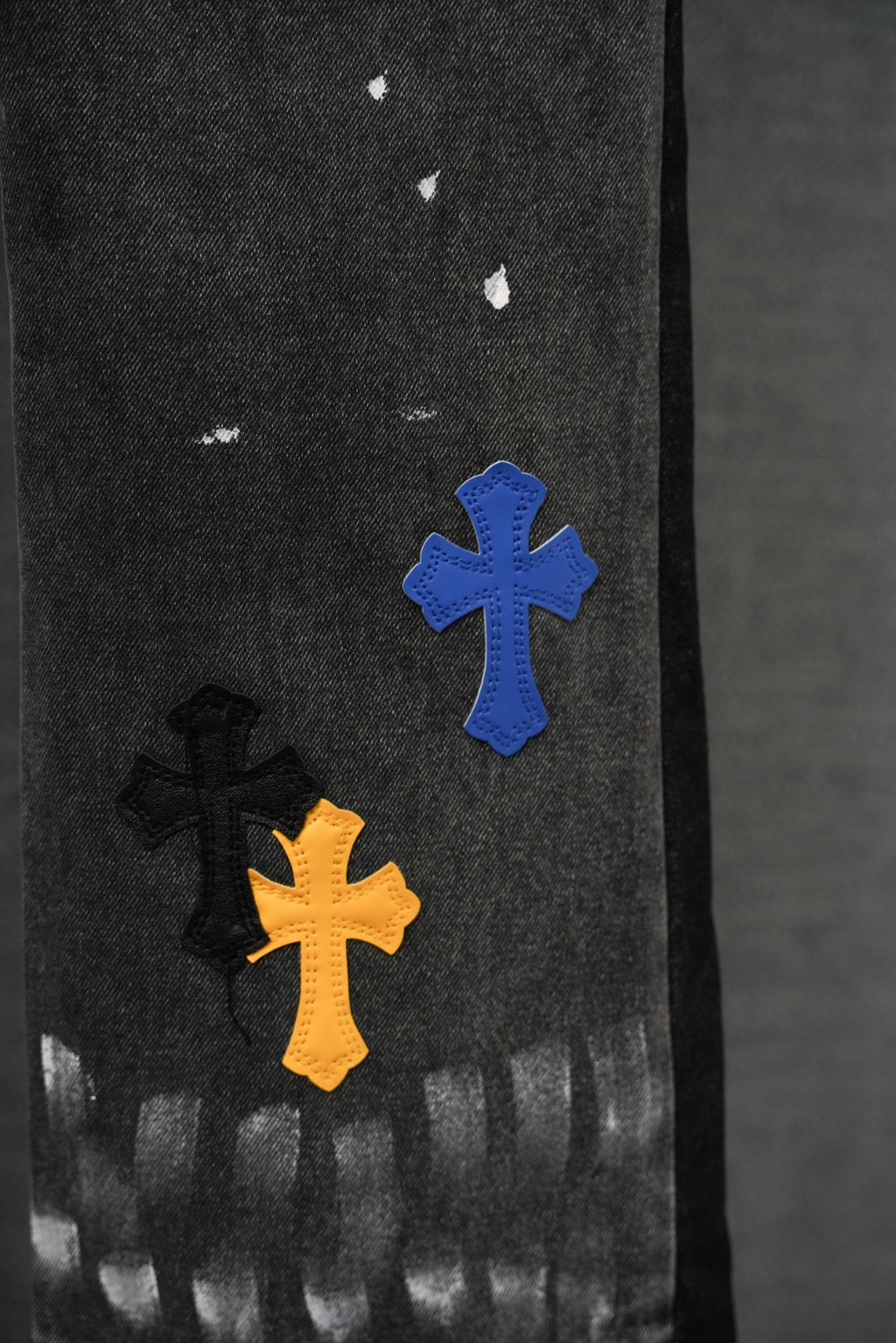 Dark denim pants with blue, orange, and black cross patches near the lower leg